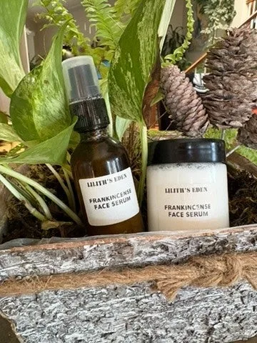 An amber pump bottle of frankincense face toner and a white jar of face serum on a stone planter