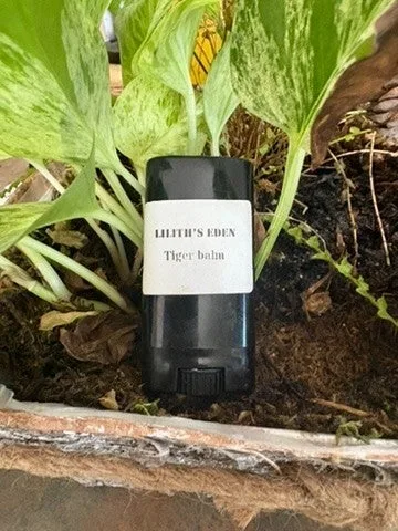 A black twist-up balm stick standing among garden leaves