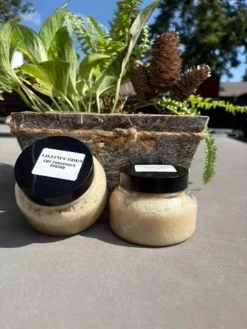 Two jars of handmade sugar scrub, one creamy and one golden, on a stone planter